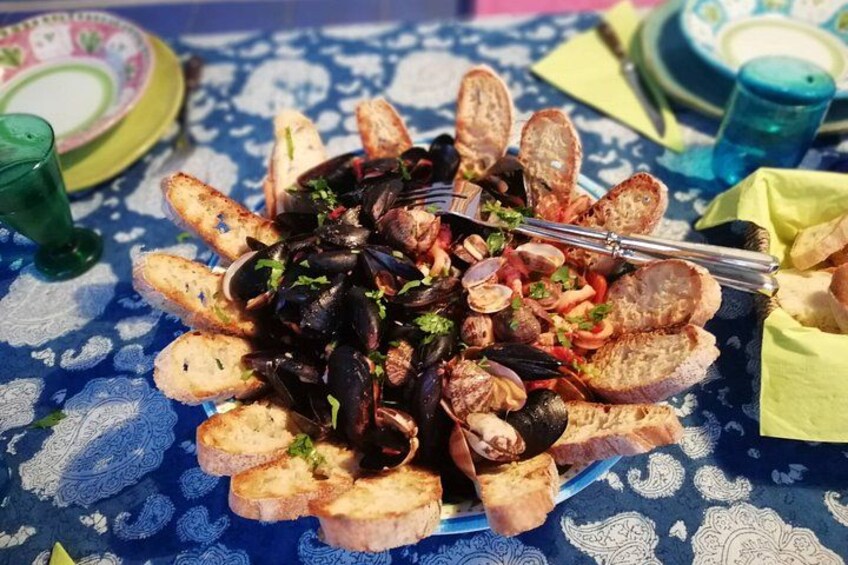 En maträtt med skaldjur, musslor och bröd, serverad på ett dukat bord. 4