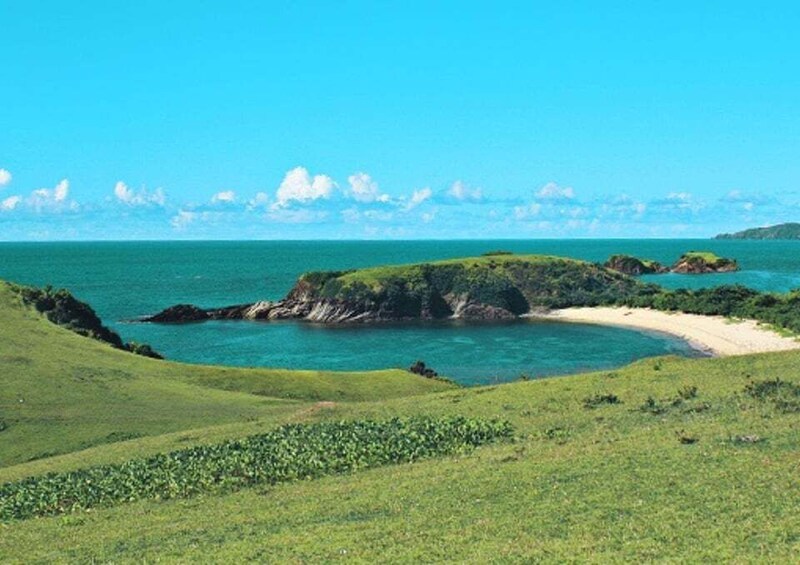 A coastal landscape with green hills, a sandy beach, and a clear blue sea. 5
