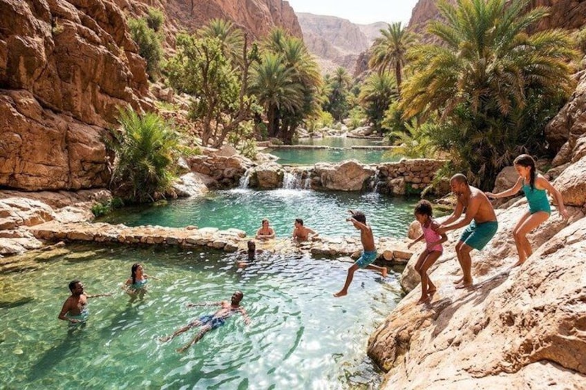 A group of people swimming and playing in a natural pool surrounded by rocky cliffs and palm trees. 2
