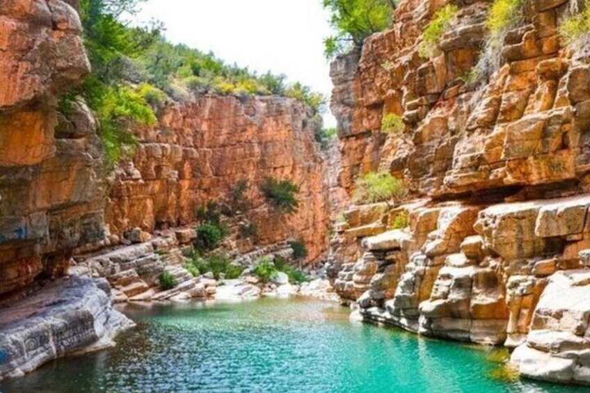 A canyon with a turquoise pool surrounded by reddish-brown cliffs and sparse vegetation. 1