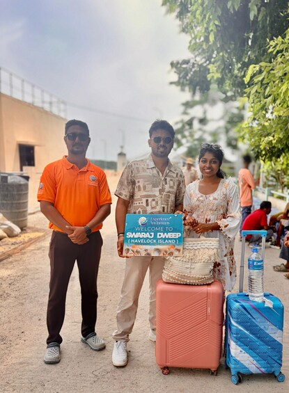 Three people standing with luggage, holding a sign that reads 'Welcome to SwaraJ Dweep (Havelock Island).' 3