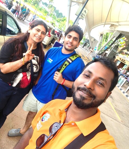 Three people outdoors, one wearing a yellow shirt with sunglasses, another in a blue shirt, and the third in a black shirt with a peace sign. 2