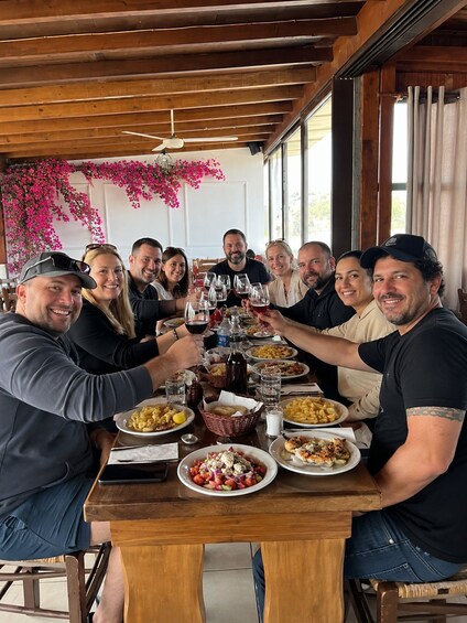 A group of people toasting at a wooden table with various dishes, surrounded by a wooden ceiling and pink flowers. 1