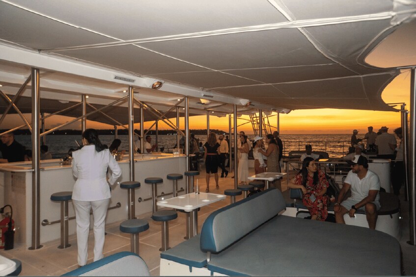 Cubierta de barco con personas cenando y una puesta de sol al fondo. 5