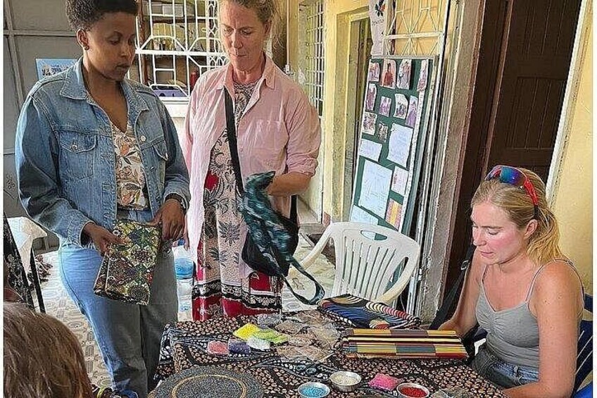 A group of people at a craft table with beads and tools. 1