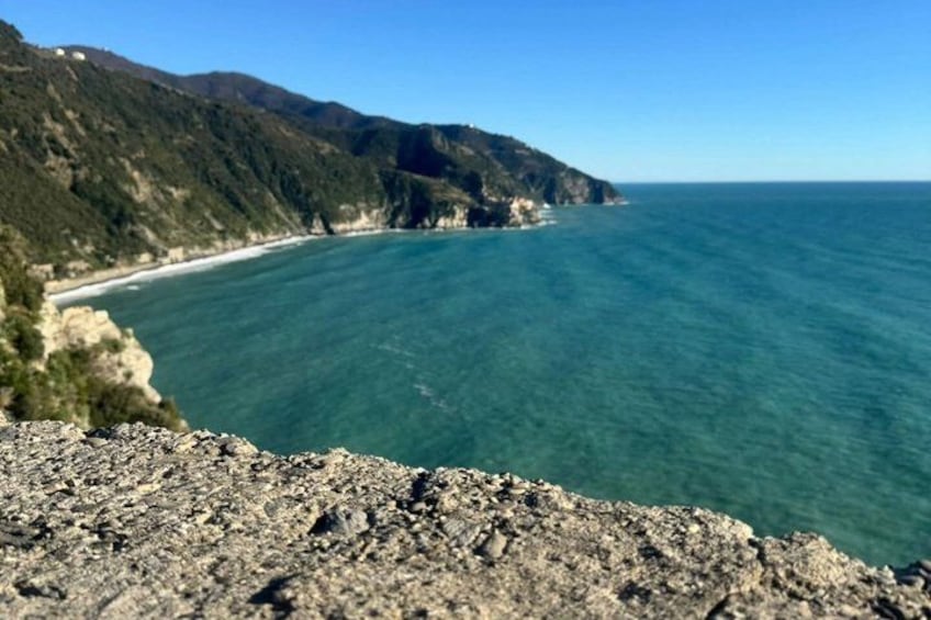 A coastal landscape with a rocky foreground, a clear blue sea, and a mountainous backdrop. 5