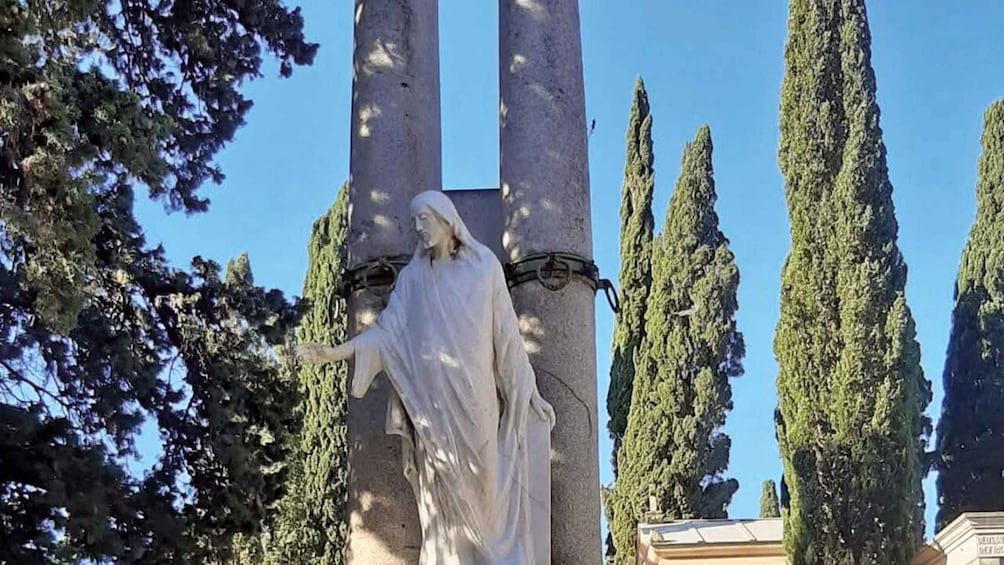 A statue of a robed figure with outstretched arms, surrounded by tall cypress trees and a clear blue sky. 5