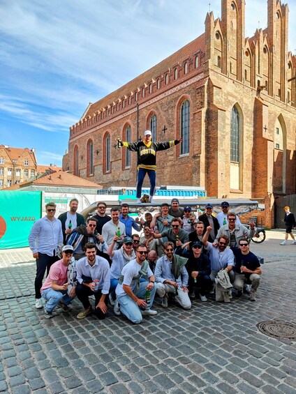 A group of people posing in front of a historic brick building with arched windows and a tower. 4