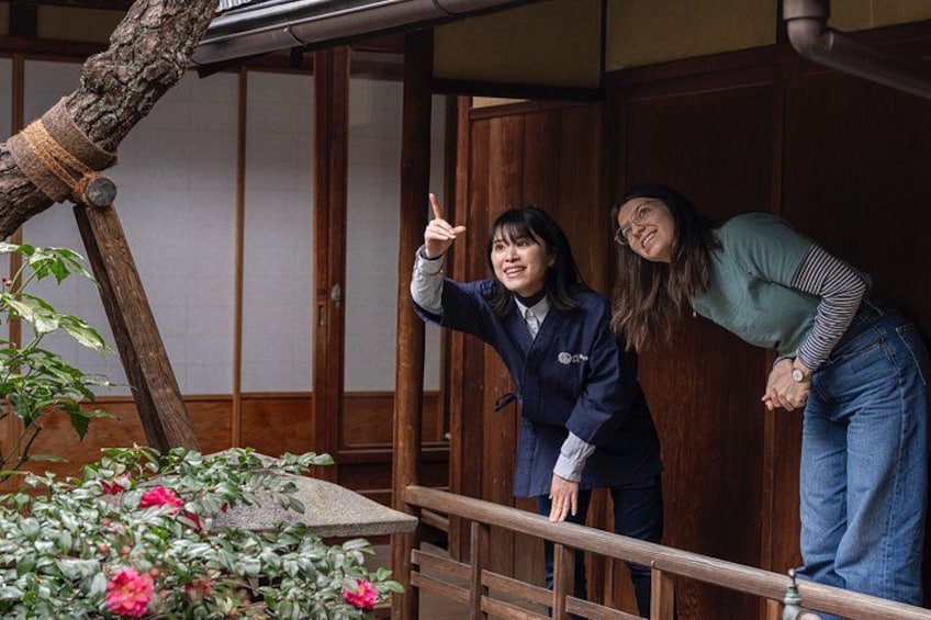 Dos personas en un balcón de madera, con un árbol y flores al frente. 5