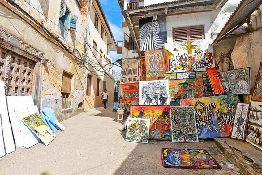Una calle estrecha con coloridas obras de arte expuestas en el suelo y las paredes, rodeada de edificios antiguos. 4