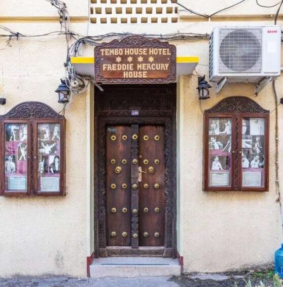Un edificio con un letrero que dice "Tembo House Hotel Freddie Mercury House" y una gran puerta de madera con manijas de latón. 3