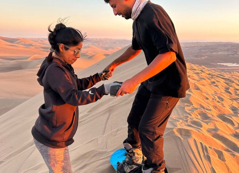 Two people on a sandy dune with a vast desert landscape in the background. 4