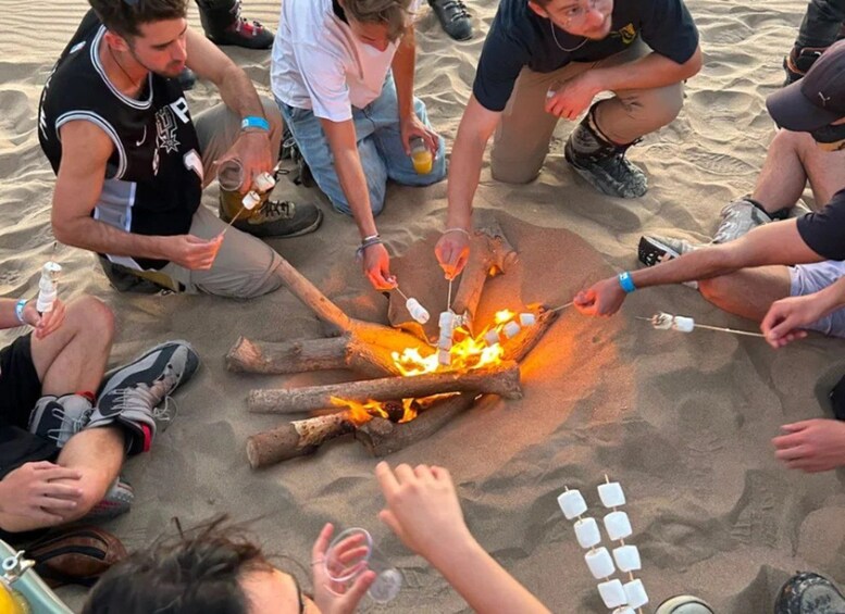A group of people roasting marshmallows over a fire on a sandy beach. 2