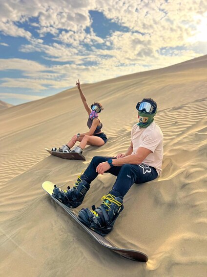 Two people snowboarding on sand dunes under a partly cloudy sky. 5