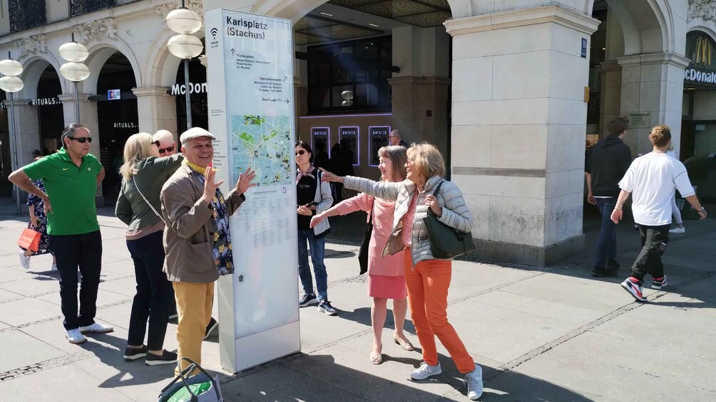 A group of people examining a large informational sign in an urban setting with historical architecture. 3