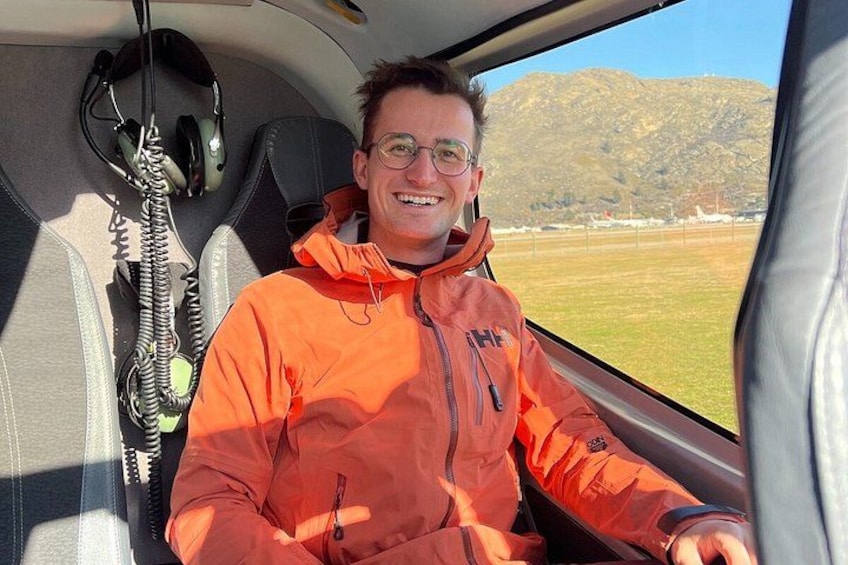 Una persona con una chaqueta naranja dentro de un vehículo, con un paisaje montañoso visible a través de la ventana. 2