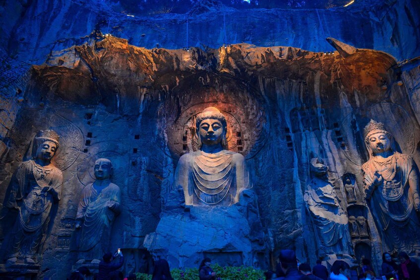 Large Buddha statues carved into a cliff face, illuminated by artificial lighting. 1