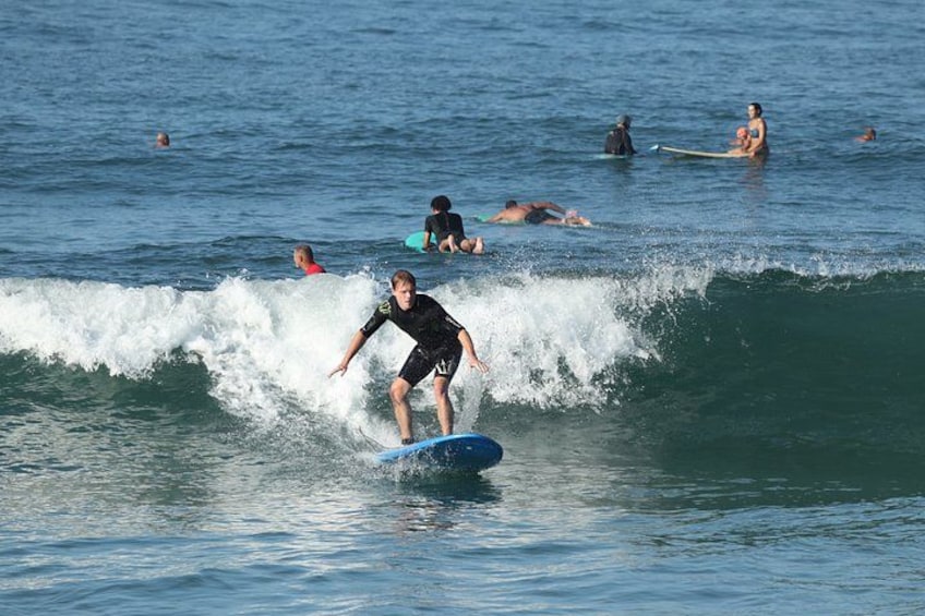 A surfer riding a wave in the ocean with other people swimming and surfing in the background. 5