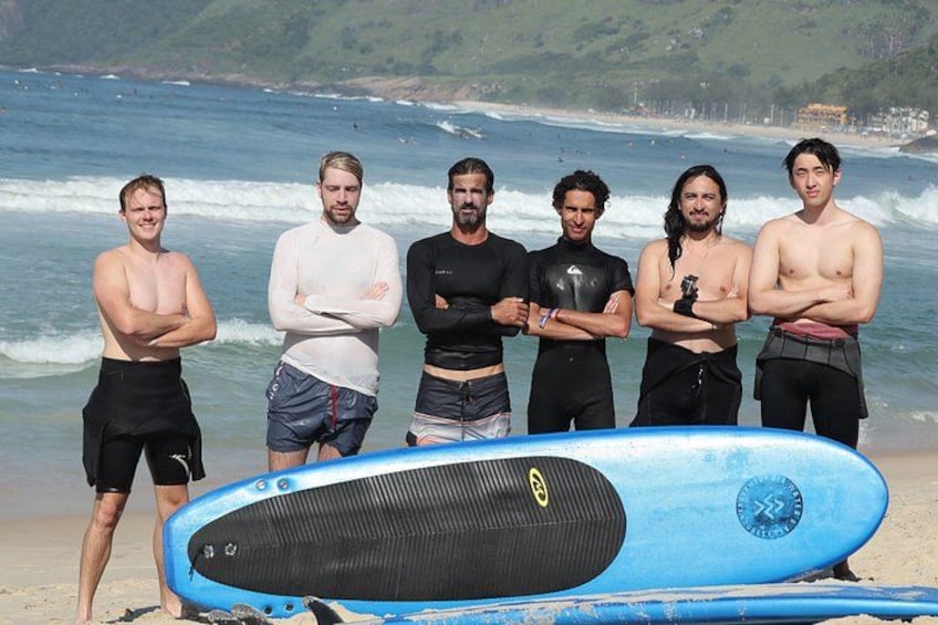 A group of people standing on a beach with a surfboard in the foreground. 4