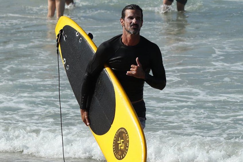 A person carrying a yellow surfboard with a black design, walking in the water. 3