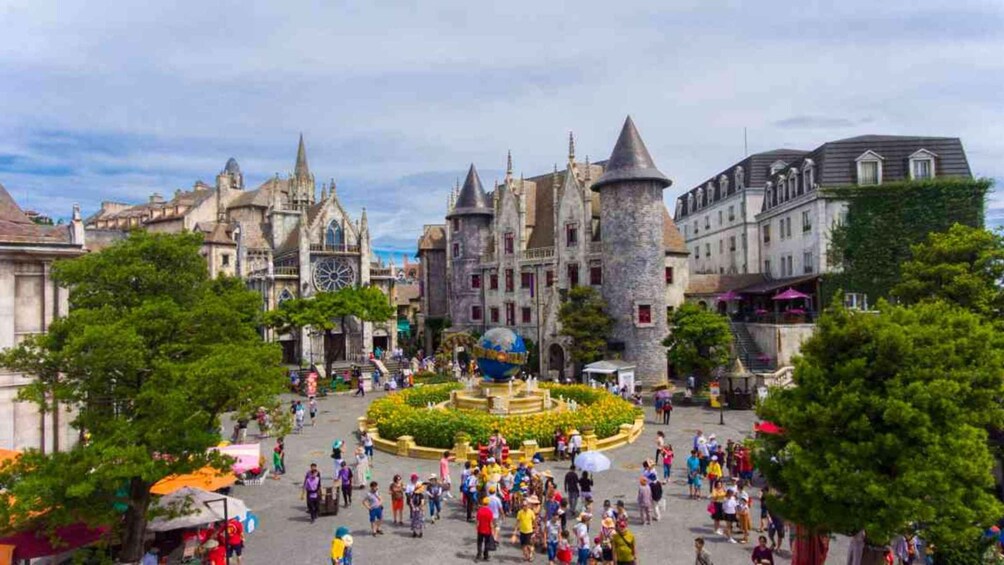 A historic castle with a central tower, a globe, and a bustling square with visitors. 4