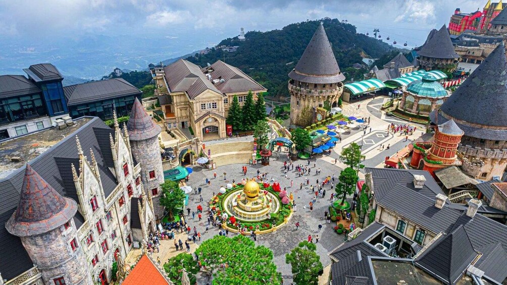 A castle-like structure with multiple towers, a central fountain, and surrounding buildings with steep roofs. 1