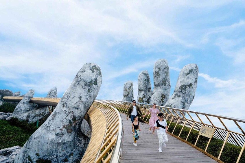 A wooden boardwalk with large rock formations resembling hands, a clear sky, and a family walking. 3