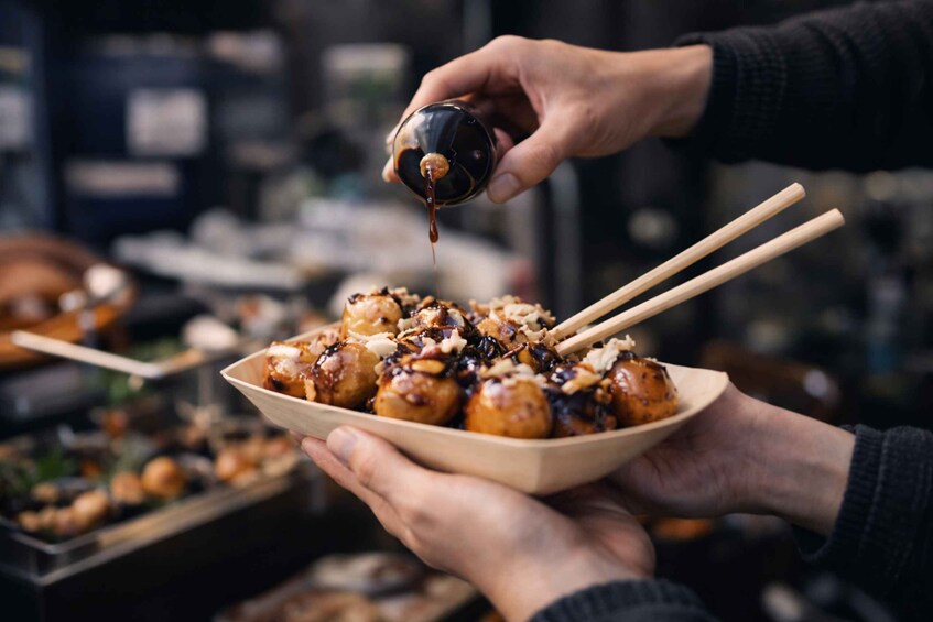 A person holding a bowl of food with chopsticks, pouring sauce over it. 2