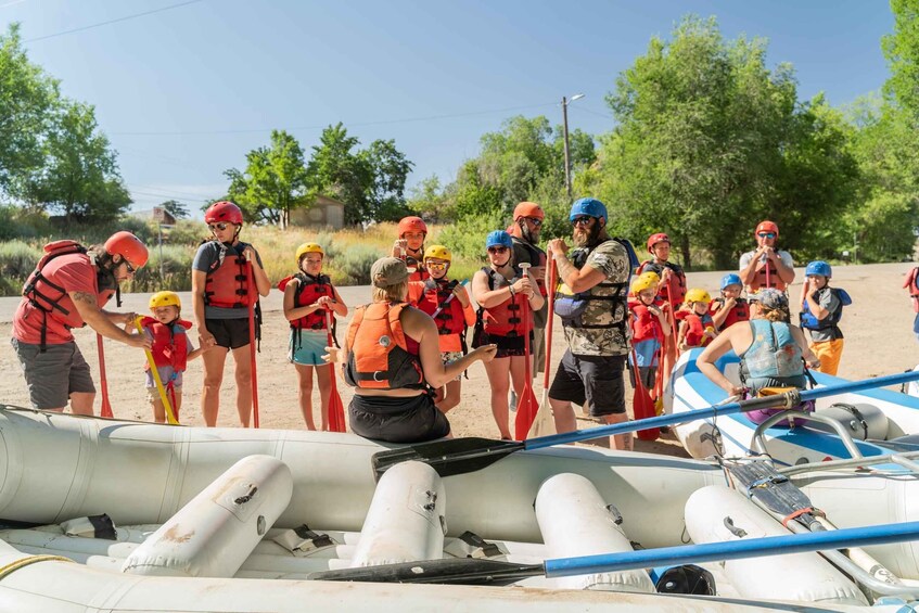 A group of people in life jackets and helmets preparing for a rafting activity on a river. 1