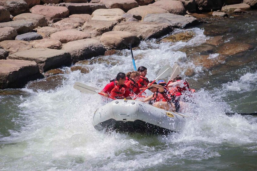 A group of people in a raft navigating through a river with rapids, surrounded by rocks. 1