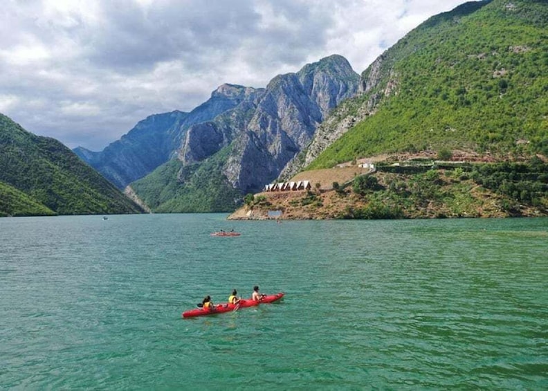 A group of people kayaking on a calm lake surrounded by lush green mountains. 1