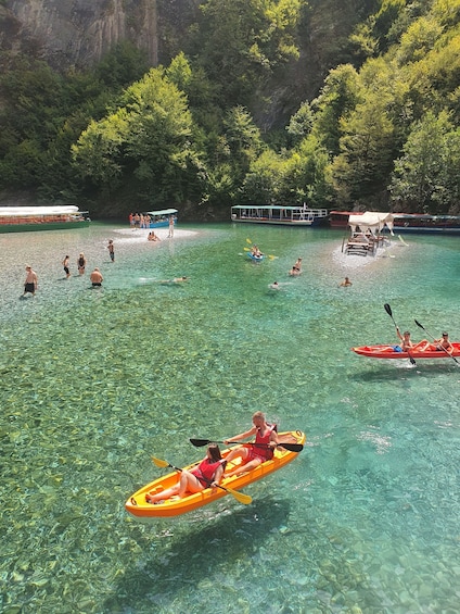 People kayaking and swimming in a clear lake surrounded by forested cliffs. 2
