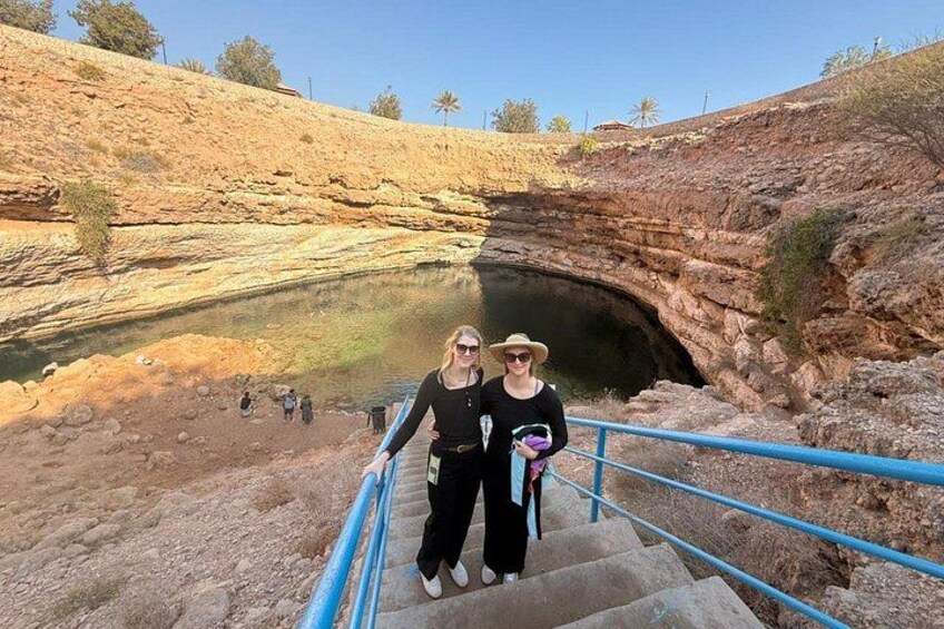 A natural rock formation with a cave entrance, a staircase leading down, and a group of people in the background. 5