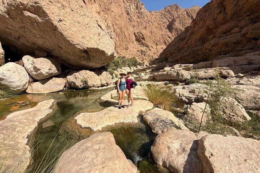 A rocky canyon with a small stream and two people standing on rocks. 5