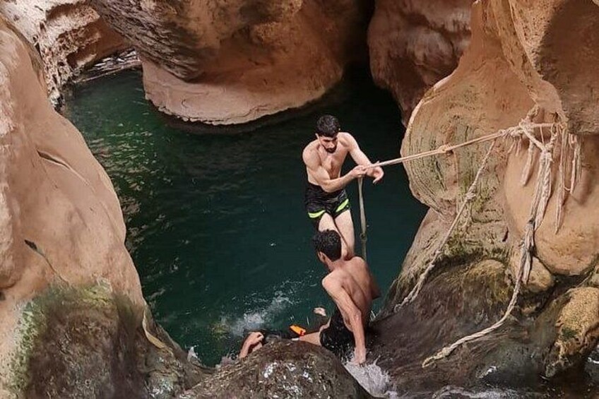 A person rappelling down a rocky cliff into a body of water. 4