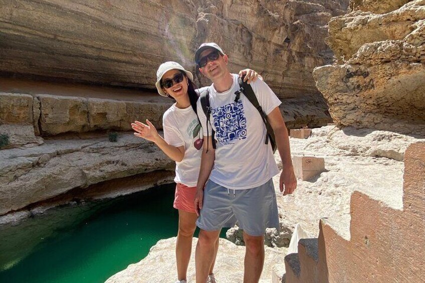 Two people standing near a rocky cliff with a green pool below. 4