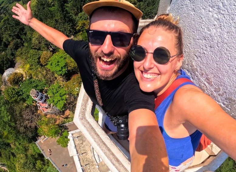 A person taking a selfie with a camera on a ledge overlooking a forested area. 3