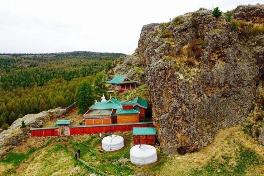 A traditional yurt settlement on a hillside with yurts and a large rock formation in the background. 2