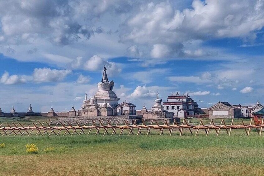 A traditional Tibetan Buddhist temple complex with white stupas and prayer wheels, surrounded by a wooden fence. 4