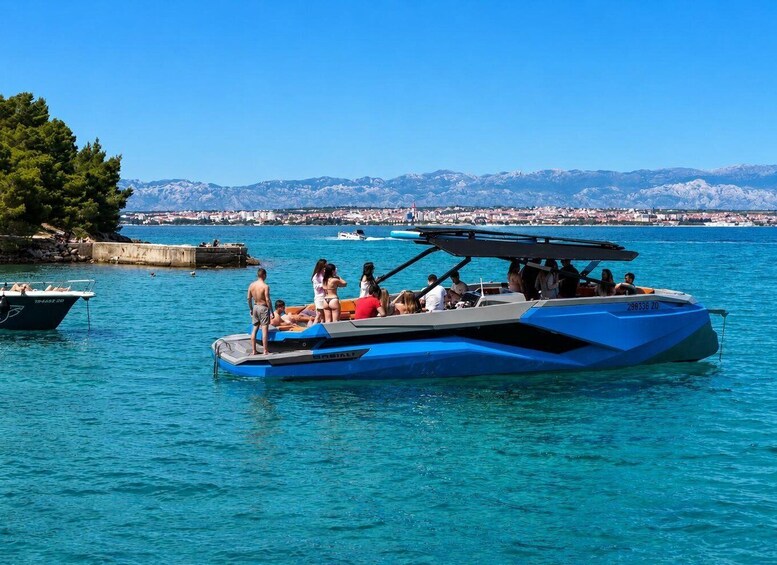 A blue boat with people on it, docked near a pier with a city and mountains in the background. 1