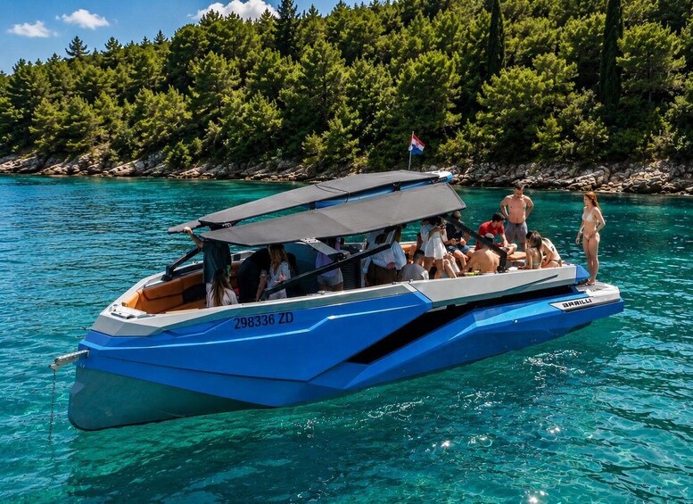 A blue motorboat with people on board, anchored near a rocky shoreline with trees. 2