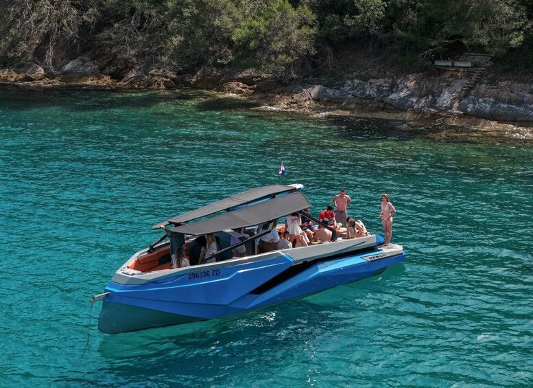 A blue speedboat with passengers, anchored near a rocky shoreline. 1