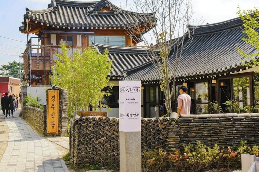A traditional Korean building with a tiled roof, a stone wall, and a signboard. 3
