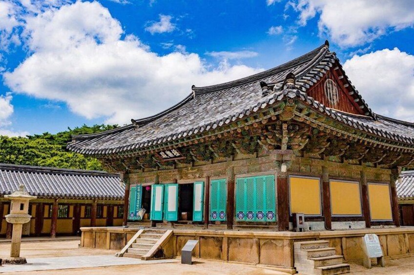 Un edificio tradicional coreano con tejado de tejas, puertas verdes y amarillas, y una escalera de piedra que conduce a la entrada. 4