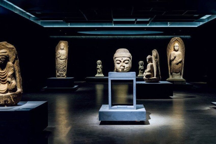 Une exposition de musée présentant des statues en pierre et un écran numérique. 4