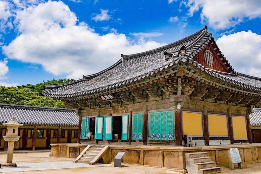 Een traditioneel Koreaans gebouw met een pannendak, groene en gele deuren, en een stenen trap naar de ingang. 2