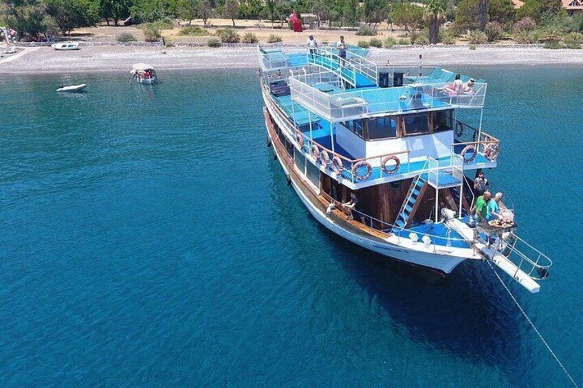 Een grote blauw-witte boot met meerdere dekken, afgemeerd aan een strand met helderblauw water. 4