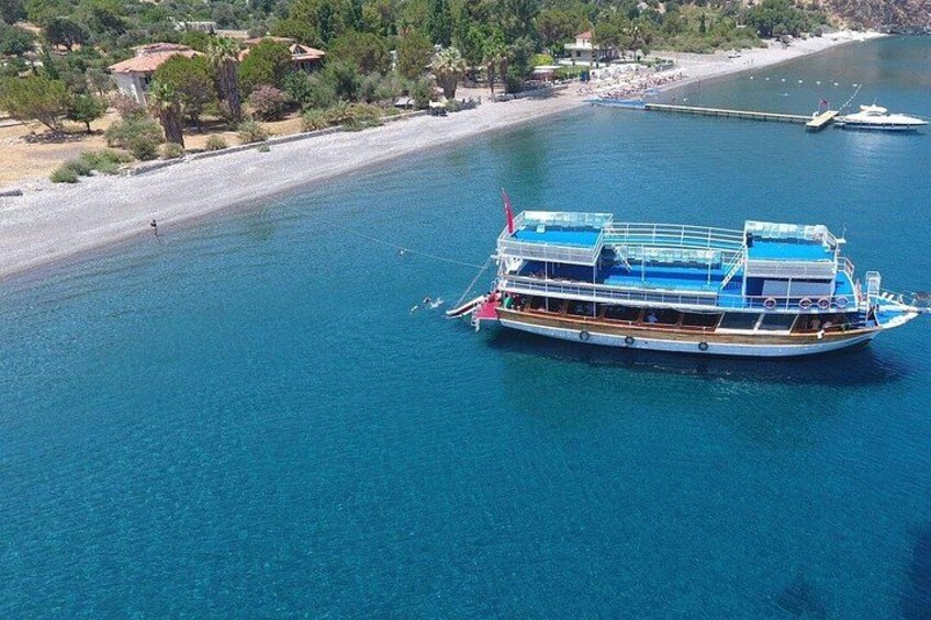 Un'ampia imbarcazione su un mare blu e limpido, con una spiaggia e alberi sullo sfondo. 4