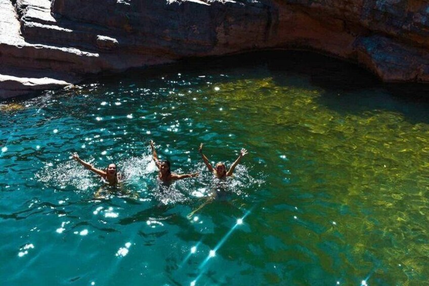 Tres personas nadando en una piscina azul y transparente, con acantilados rocosos al fondo. 4