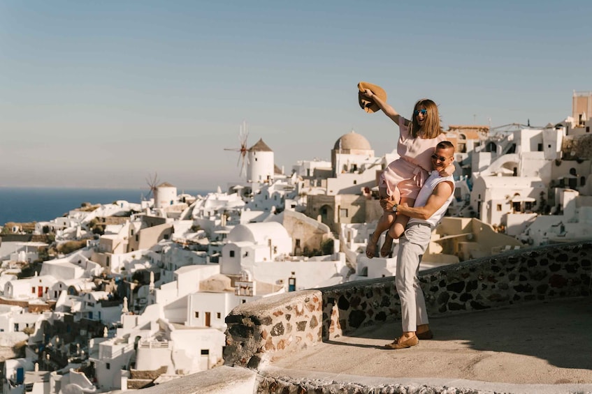 A man carrying a child on his shoulders, overlooking a white-washed village with windmills and domed buildings. 5